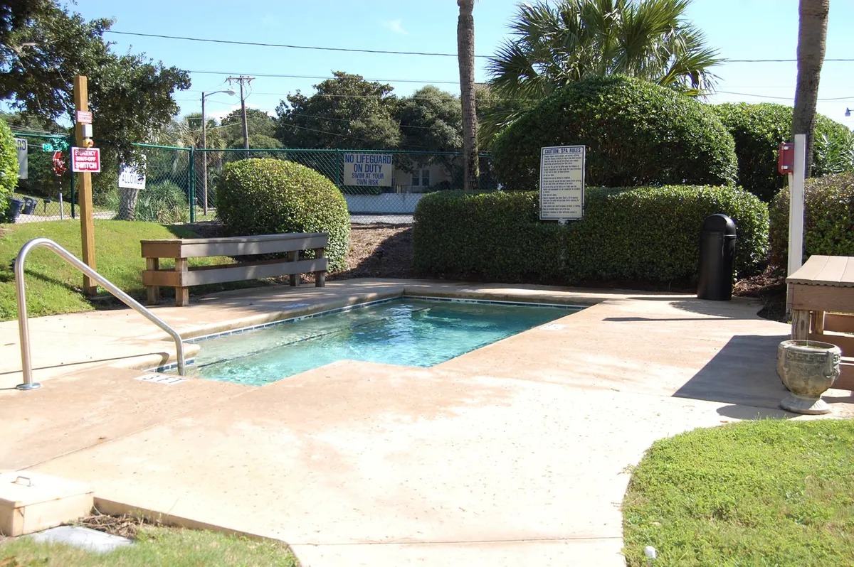 This image presents an inviting outdoor pool surrounded by benches and lush greenery. The calm water and sunny atmosphere suggest a space perfect for both family fun and relaxation. The setting is open, clean, and appealing, with ample seating for guests to socialize or unwind.