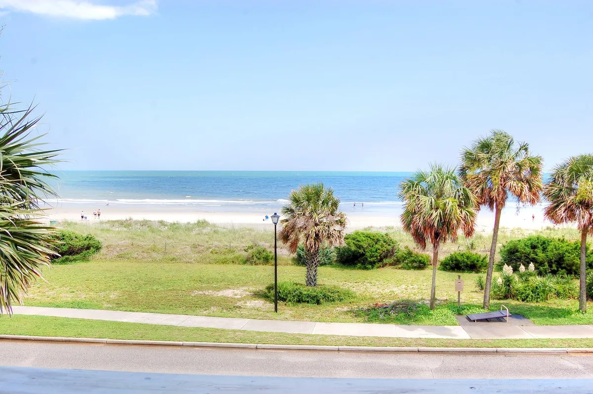 This image features a sweeping view of Myrtle Beach, golden sand, and gentle ocean waves. Palm trees frame a pathway leading directly to the shoreline, while families and children enjoy activities like building sandcastles, sunbathing, and splashing in the surf.