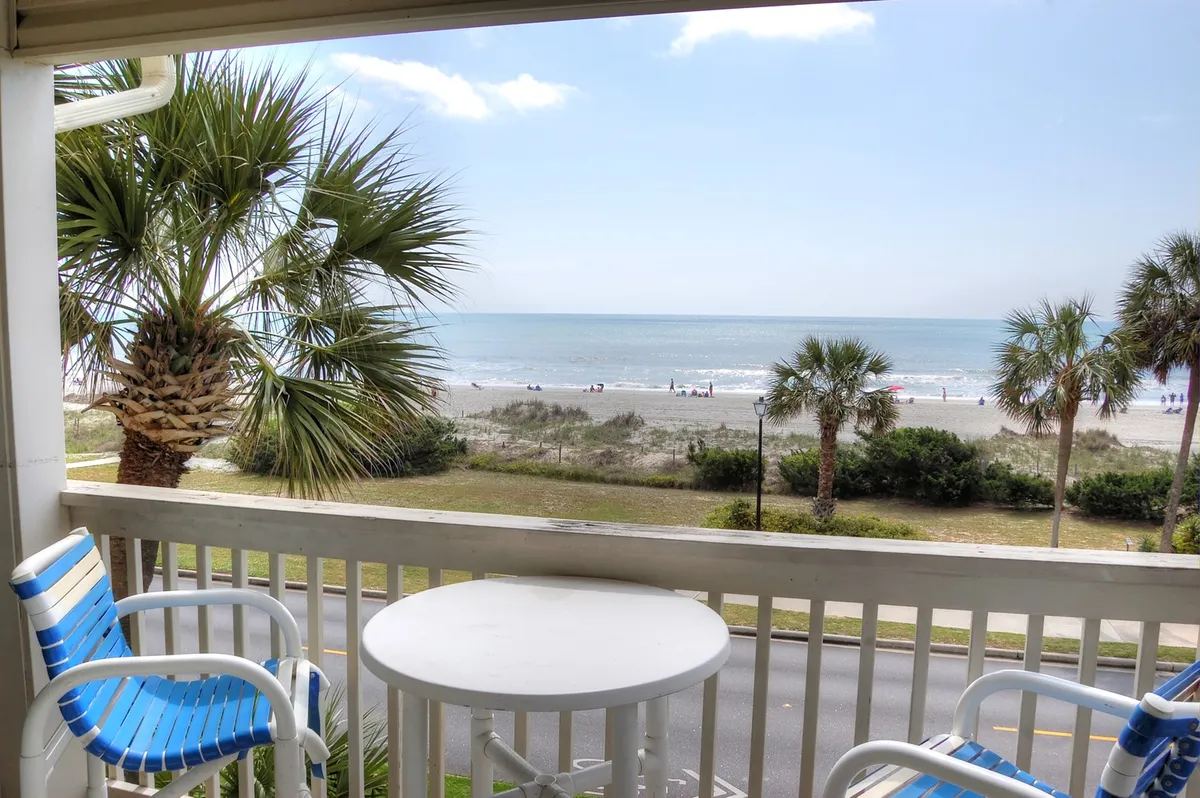 The image showcases a private balcony overlooking the sparkling Atlantic Ocean, framed by swaying palm trees. Comfortable outdoor furniture invites guests to unwind while taking in breathtaking sunrise views and the soothing sounds of the waves.