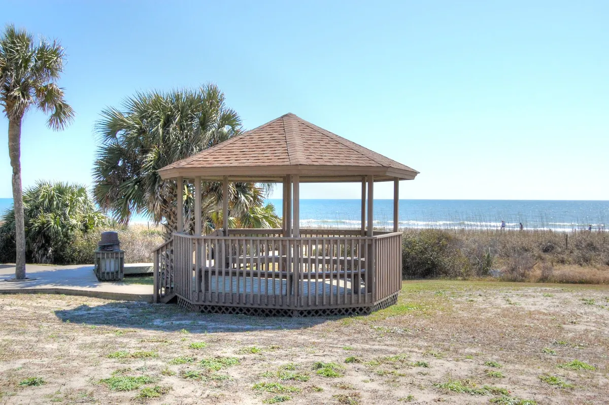 A peaceful exterior scene with a wooden gazebo overlooking the ocean, framed by palm trees. The setting invites relaxation, with potential for picnics, morning coffee, or quiet conversation while enjoying the sea breeze and panoramic views.