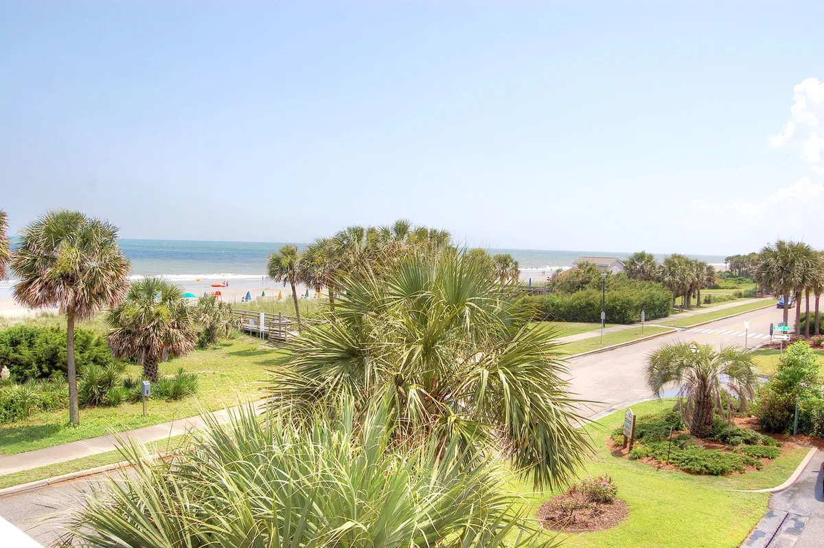 A serene, wide-angle ocean view from the shore, featuring sandy beach, palm trees, and a gently curving pathway. The tranquil beach scene suggests opportunities for morning walks, sunset strolls, and quiet contemplation by the water—activities appealing to couples and friends on a getaway.