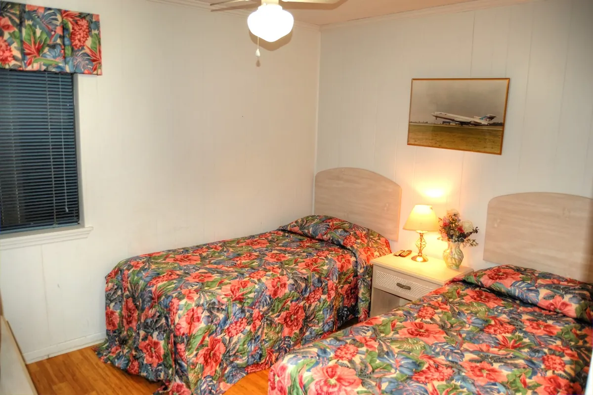This image captures a cheerful and relaxed bedroom with floral bedspreads, a nightstand with a lamp, and playful wall art of an airplane. The twin beds offer a comfortable and inviting space, ideal for family or friends sharing the room.