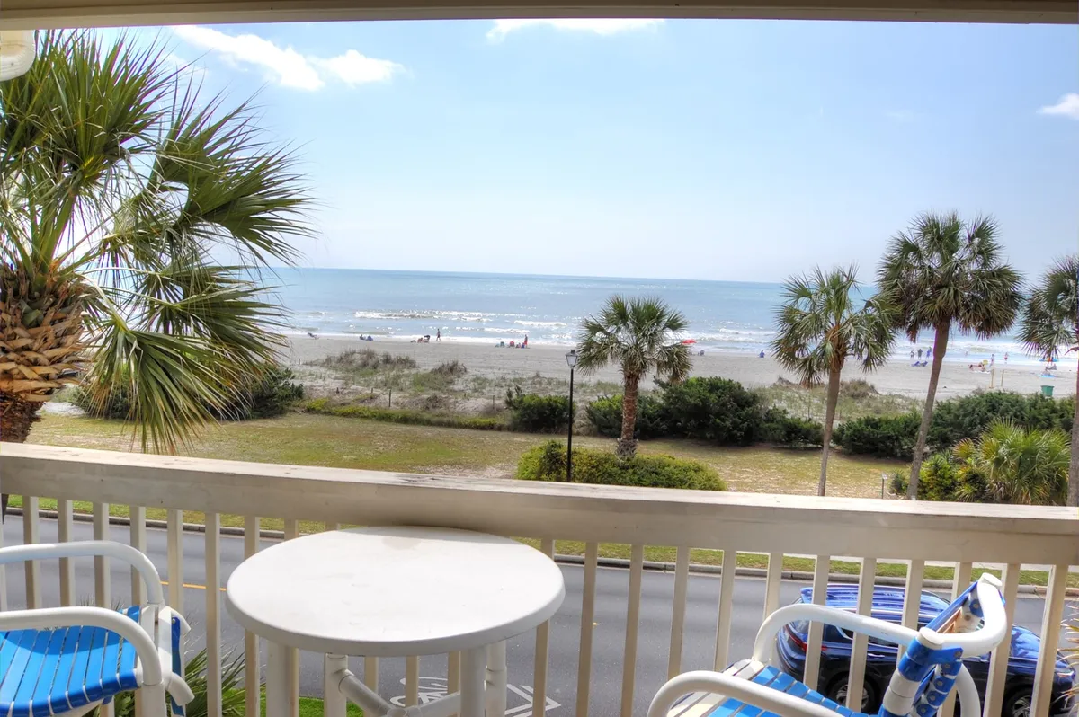 A stunning ocean view from a balcony with palm trees and beachgoers in sight. The tranquil scene captures the proximity to the ocean and invites natural light and scenic beauty into the living space.
